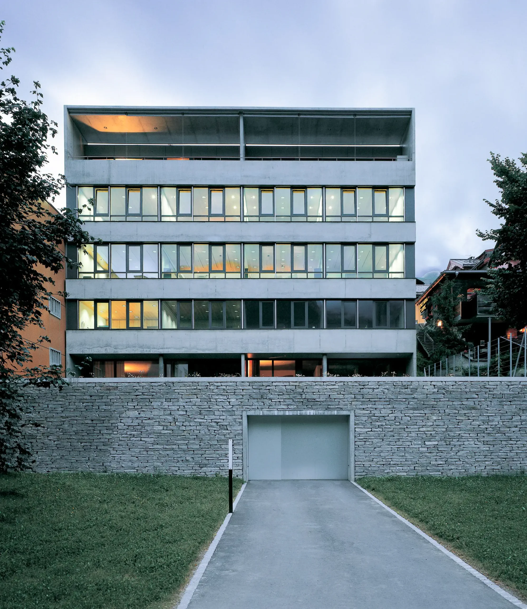 GKB Scuol Fassade Süd Fensterfront und Eingang Tiefgarage mit Natursteinmauer