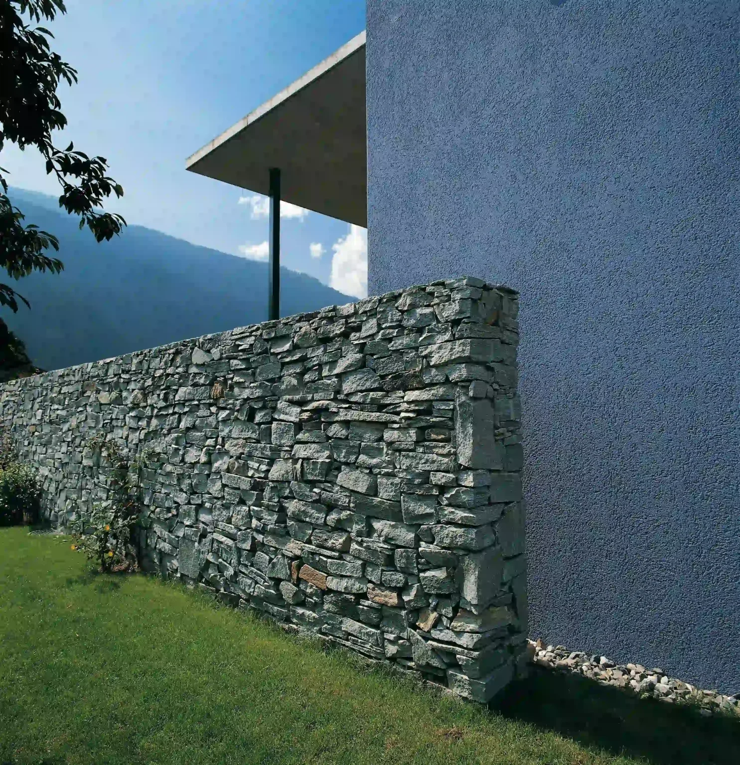 Wohnhaus Cavigelli DomatEms Natursteinmauer Garten und Sichtbetonvordach